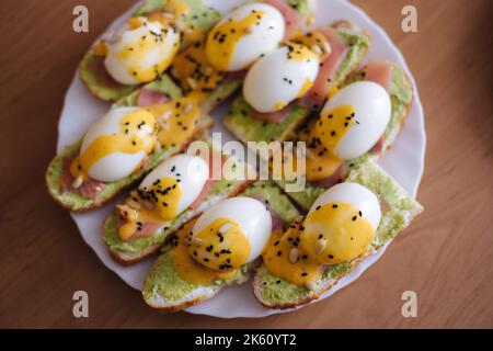 Ein köstliches Ei benedikt mit geräuchertem Lachs, Sauce Hollandaise, Guacamole, Pinien-Nüsse und schwarzem Kreuzkümmel bestreut. Draufsicht Stockfoto