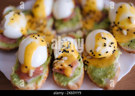 Delikat Toast mit Lachs, gekochtem Ei und Guacamon auf einem weißen Platt bestreut Pinienkernen und schwarzem Kreuzkümmel. Stockfoto