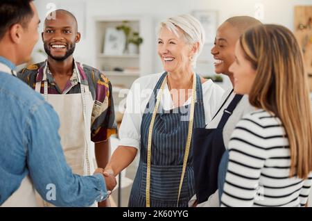 Eine Gruppe von glücklichen, vielfältigen kreativen Designern, die sich bei der Arbeit treffen. Fröhliche Kollegen begrüßen und schütteln die Hände in einem Stockfoto