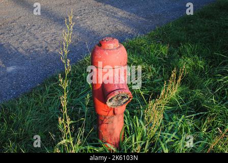 Nahaufnahme eines alten roten Hydranten auf Gras in der Nähe einer Straße Stockfoto