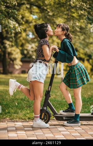 Hübsche junge Mädchen im Park reiten einen Roller und genießen Stockfoto