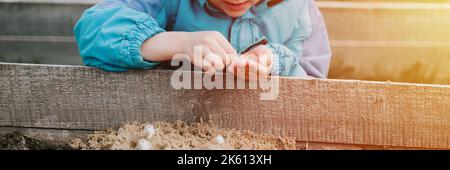 Frühling Pflanzung Aussaat im Bauerngarten. Kleine sechs Jahre alte Kind Junge Bauer Gärtner Pflanzen und säen Gemüsesamen im Boden im Bett. Gartenarbeit und Summe Stockfoto