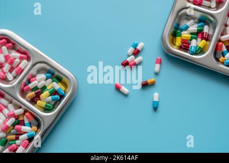 Mehrfarbige Kapseln in Edelstahlschale und auf blauem Hintergrund. Apothekenbanner. Pharmaindustrie. Pharmazie. Verschreibungspflichtiges Medikament Stockfoto