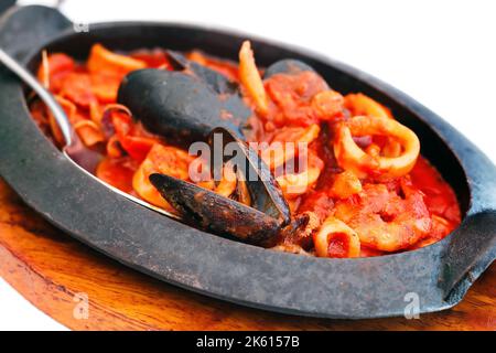 Muscheln, Calamari und Garnelen mit Tomatensauce in einer gusseisernen Schale gebacken (selektiver Fokus) Stockfoto