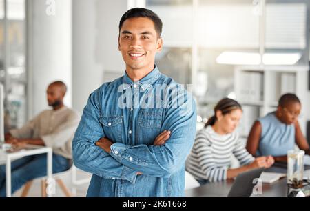 Junger glücklicher gemischter Geschäftsmann, der in einem Büro mit gekreuzten Armen steht. Selbstbewusster und zufriedener hispanischer männlicher Chef, der lächelt und ansteht Stockfoto