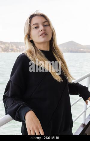 Junge blonde Frau in schwarzem Pullover, die von der Fähre über den bosporus in istanbul auf die Kamera schaut, Stockbild Stockfoto