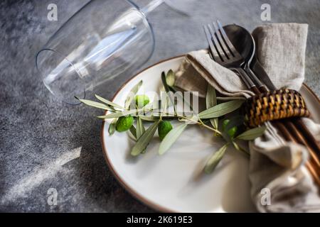 Rustikales Sommertischgeschirr mit Teller und Besteck, dekoriert mit Olivenbaumbästen Stockfoto