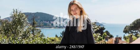 Junge und blonde Frau posiert in der Nähe von Häusern und Meer auf Prinzessin Inseln in der türkei, Banner, Stockbild Stockfoto