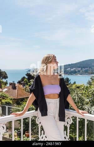 Junge und blonde Frau posiert in der Nähe von Gebäuden und Meer auf Prinzessin Inseln in der türkei, Stockbild Stockfoto