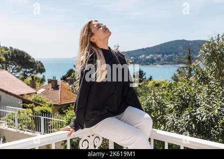 Erfreut und blonde Frau posiert in der Nähe von Häusern und Meer auf Prinzessin Inseln in der türkei, Stockbild Stockfoto