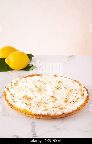 Von oben wird tagsüber leckere Meringue-Tarte auf einem Marmortisch in der Nähe von Zitronen serviert Stockfoto