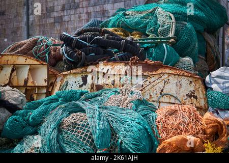 Ein Haufen Fischernetze, die tagsüber im Hafen auf korrodiertem Metall gegen eine Ziegelmauer gelegt wurden Stockfoto