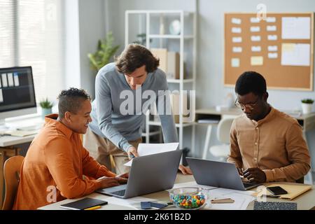 Portrait eines kreativen Geschäftsteams, das im Büro zusammenarbeitet, Schwerpunkt auf der Beratung junger Männer mit Kollegen Stockfoto