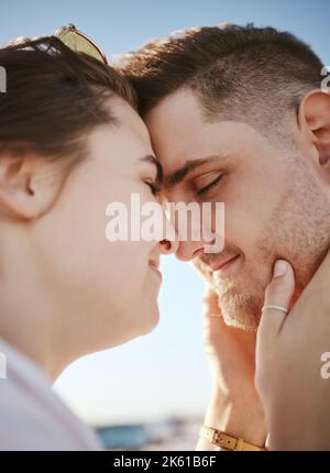 Liebe, berührendes Gesicht und Paar am Strand, Frau hält Mann mit Köpfen zusammen. Sommer, Romantik und liebevolles glückliches Paar im Urlaub. Echte Menschen Stockfoto