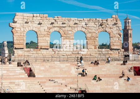 Verona, Blick im Sommer auf die verbleibenden vier Bögen der Außenwand der römischen Arena mit Touristen im Amphitheater sitzen, Verona, Italien Stockfoto