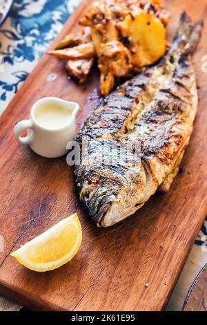 Gegrillte Seebrasse auf einer rustikalen Holzplatte mit einer Seite von Süßkartoffeln und Tartarsauce serviert, selektive Fokus Stockfoto