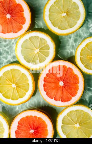 Vertikales buntes Hintergrundbild von Zitrusfrüchten Zitrone, Orange, Grapefruit, Scheiben in Wasser spritzt frische transparente Oberfläche mit Flecken. Flach Stockfoto