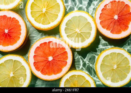 Buntes Hintergrundbild von Zitrusfrüchten Zitrone, Orange, Grapefruit, Scheiben in Wasser spritzt frische transparente Oberfläche mit Flecken. Flach liegend, oben Stockfoto