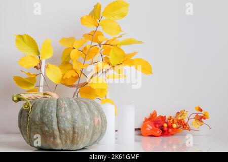 Herbstdekor aus Kürbissen, Ästen mit Blättern, Kerzen auf einem weißen Tisch. Thanksgiving oder Halloween Konzept. Stockfoto