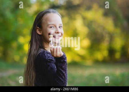 Nettes Mädchen saugen auf einem Lutscher Süßigkeiten. Herbstpark im Hintergrund. Stockfoto