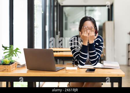 Müde asiatische männliche Student sitzen am Schreibtisch mit Laptop. Gelangweilte Jugendliche sind erschöpft von der Vorbereitung auf Tests oder dem Schreiben von Kursarbeiten und fühlen sich müde Stockfoto