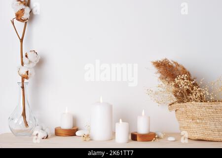 Dekoration mit Kerzen, Korb und Blumen über der weißen Wand. Interior Design Konzept. Nahaufnahme, Kopierbereich Stockfoto