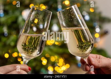 Paar hält Gläser Champagner gegen den Weihnachtsbaum. Happy New Year Party Konzept. Stockfoto
