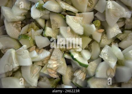 Viele in Scheiben geschnittene 1/4 reife Gurken stapelten sich in eine große weiße Salatschüssel. Nützliches Gemüse, gesunde Ernährung, Hintergrund von Gurken in Scheiben geschnitten mit Samen. Stockfoto