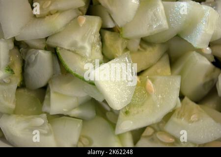 Viele in Scheiben geschnittene 1/4 reife Gurken stapelten sich in eine große weiße Salatschüssel. Nützliches Gemüse, gesunde Ernährung, Hintergrund von Gurken in Scheiben geschnitten mit Samen. Stockfoto