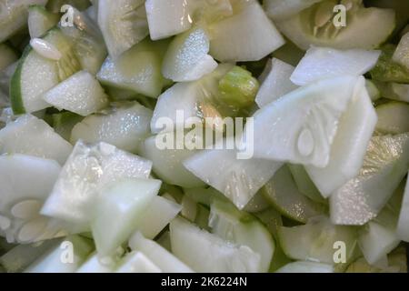 Viele in Scheiben geschnittene 1/4 reife Gurken stapelten sich in eine große weiße Salatschüssel. Nützliches Gemüse, gesunde Ernährung, Hintergrund von Gurken in Scheiben geschnitten mit Samen. Stockfoto