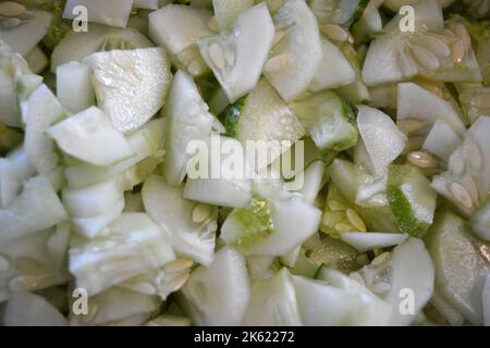 Viele in Scheiben geschnittene 1/4 reife Gurken stapelten sich in eine große weiße Salatschüssel. Nützliches Gemüse, gesunde Ernährung, Hintergrund von Gurken in Scheiben geschnitten mit Samen. Stockfoto