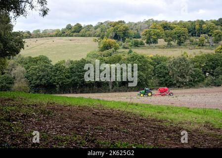 Ein grüner Traktor mit einem roten Anhänger, der an einem Herbsttag in England auf dem Surrey Hill bei Abinger Roughs in der Nähe von Dorking auf einem Feld arbeitet Stockfoto