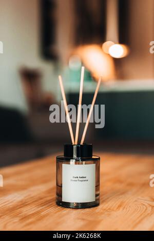 Stilvolle Glasflasche mit Duftdiffusoren aus Holzstäbchen auf Holztisch. Heimtextilien. Minimalistisches Lufterfrischer-Konzept. Duft nach Hause Stockfoto