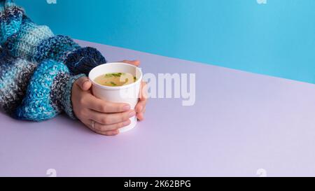 Hände mit einer Tasse zum Mitnehmen und Hühnerbrühe Stockfoto