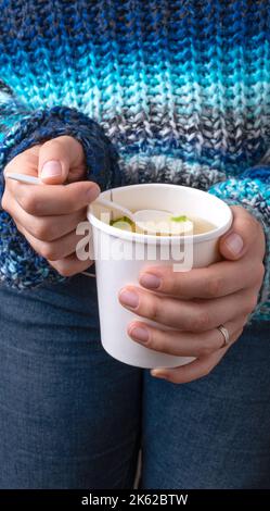 Hände mit einer Tasse zum Mitnehmen und Hühnerbrühe Stockfoto