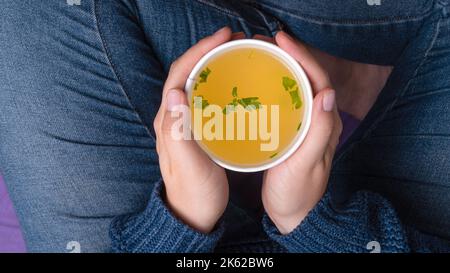 Hände mit einer Tasse zum Mitnehmen und Hühnerbrühe Stockfoto