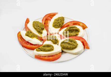 Mozzarella mit Tomaten und Pesto in der Nähe auf weiß. Leichter erfrischender Caprese-Salat mit frischen Mozzarella und reifen Tomaten, italienische Vorspeise oder Stockfoto