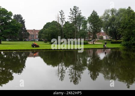 Kortrijk, Westflandern Region - Belgien - 07 10 2021 Wasserteichspiegelungen im Stadtpark Raemdonck mit einem Mann beim Angeln und einem Mähen Stockfoto