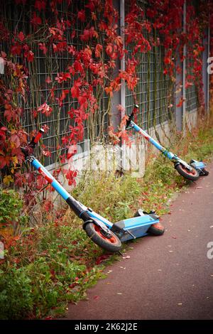Eine vertikale Aufnahme von zwei gemieteten Elektrorollern, die auf einem Zaun an der Seite einer Reihe gelehnt sind Stockfoto