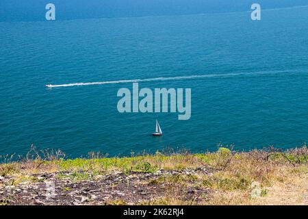 Ein Blick auf das Meer von der Howth Dublin, ein Boot segelt und ein anderes macht eine weiße Flugbahn, blauer, wolkigen Himmel Hintergrund, Irland Stockfoto