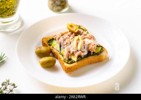 Toast mit Thunfisch und Avocado, Oliven mit Chimichurri-Sauce. Auf einem weißen Teller und weißem Hintergrund. Stockfoto