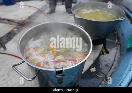 Details zur geringen Schärfentiefe (selektiver Fokus) mit einem großen Metallkessel, in dem eine traditionelle rumänische Fischsuppe (Ciorba de peste) coo ist Stockfoto