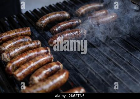 Details zu geringer Schärfentiefe (selektiver Fokus) bei Schweinefleischwürsten, die auf einem Barbecue-Grill in einem europäischen Bauernmarkt gekocht werden. Stockfoto