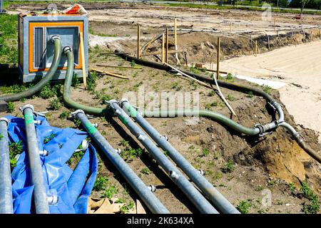 Große tragbare elektrische Wasserpumpe mit Schlauch zur Entwässerung der tiefen Grube des Gebäudefundaments, Entwässerungssystem auf der Baustelle Stockfoto