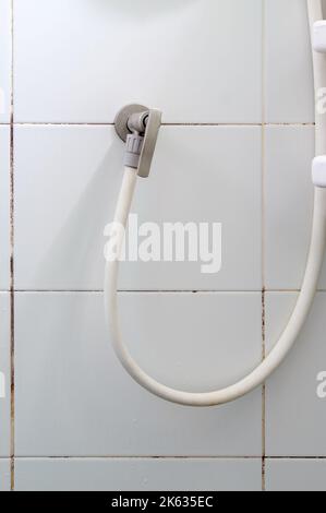 Das weiße Gummiband mit dem Messing Wasserhahn der Dusche in der Nähe der weißen Fliesenwand in der Duschkabine, Vorderansicht mit dem Kopierraum. Stockfoto