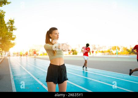 Frau Streckt Und Wärmt Die Arme Vor Dem Laufen Auf. Fit Sport Frau Stretching ihren Körper Aufwärmen Stehen auf Laufstrecke Start line bereit Joggen. Athletische Frau bereitet sich auf das Lauftraining vor Stockfoto