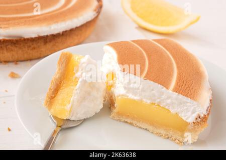 Nahaufnahme einer Portion Zitronentarte mit Baiser auf weißem Teller mit einem Schluck auf einer Gabel. Stockfoto
