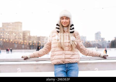 Medium Shoot Portrait der romantischen europäischen Dame trägt stilvolle Winterjacke und lustige flauschige Hut in verschneiten Tag. Foto im Freien von inspirierter blonder Frau, die Freizeit in der Winterstadt genießt. Weihnachten Stockfoto