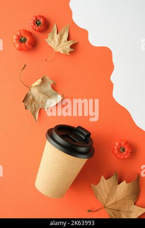 Kaffeebecher mit Naturkorkband. Kaffeetasse auf orange-weißem Herbsthintergrund mit trockenen Platanenblättern und Deko-Kürbissen. Flach liegend, vertikal Stockfoto