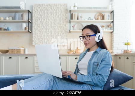 Asiatische Frau, die zu Hause auf dem Sofa sitzt und mit einem Laptop Bildungsvideos anschaut, Student, der ferngesteuert online studiert. Stockfoto